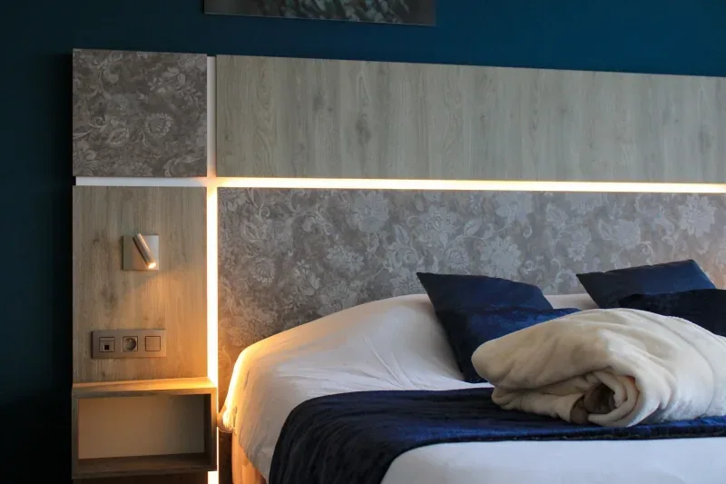 A standard bedroom in deep blue with the bed made up and towels laid out
