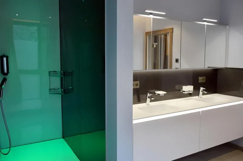 An italian shower lit in green next to a wide basin